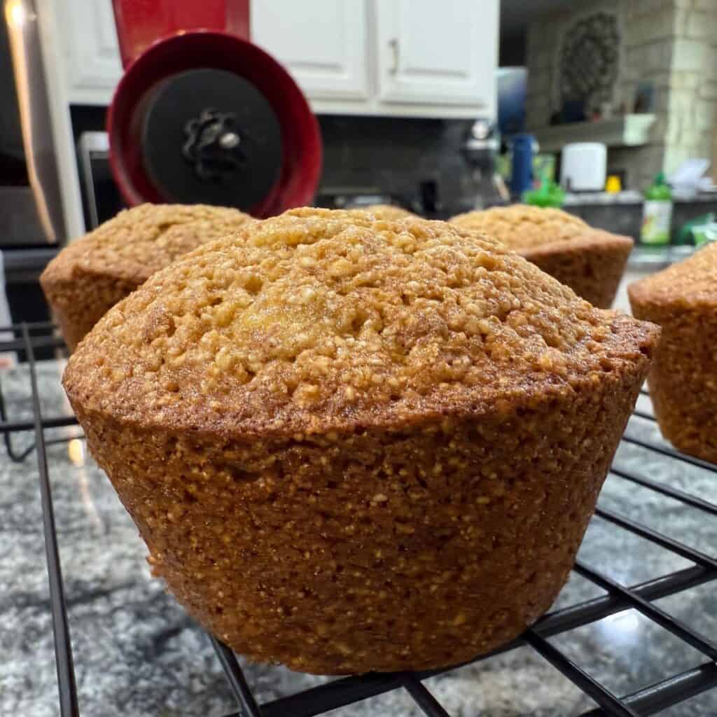 Close up of a Freshly Milled Whole Wheat Banana Muffin with a Wondermill Junior Deluxe Manual Grain Mill in the Background
