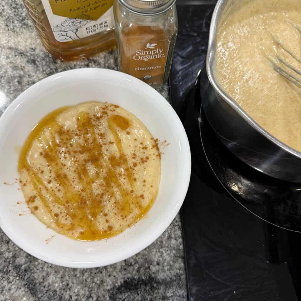A bowl of cremita (cream of wheat) made with freshly milled flour topped with honey and cinnamon sitting next to a pot of cremita on the stove